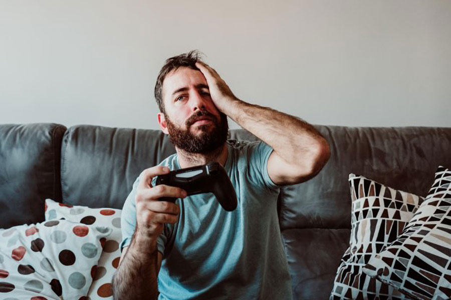 Picture of a Gamer on a couch experiencing headache while playing video games.