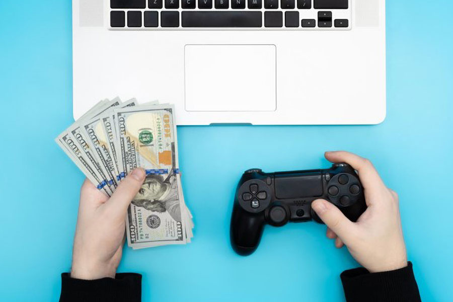 Picture of a streamer holding money and gaming controller in front of a laptop. you should really know how to make money streaming games on twitch.