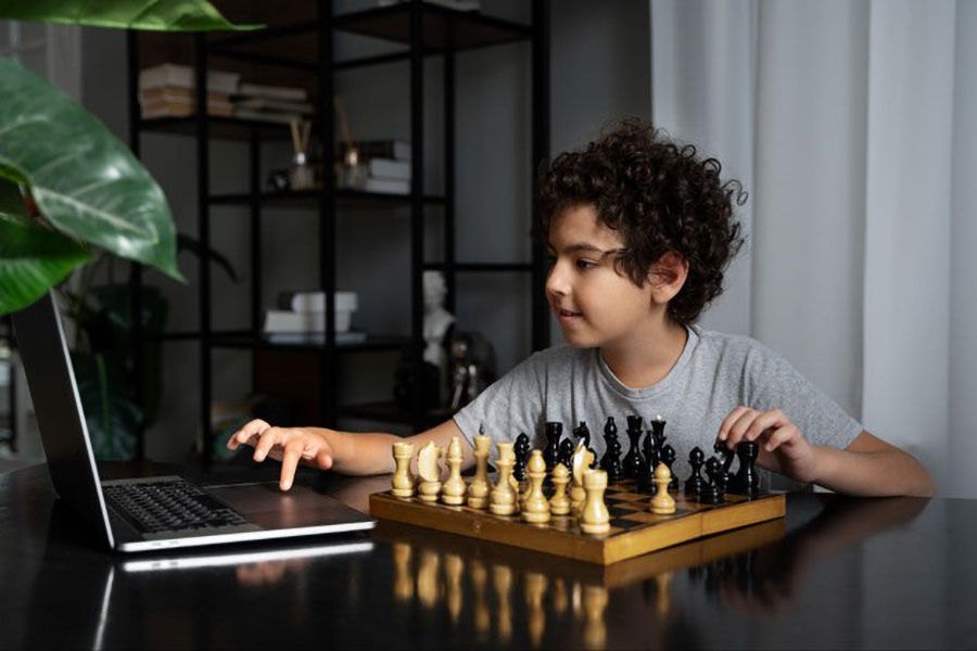 A Child playing chess while working with a laptop on a table.