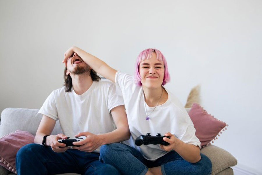 A gamer girl covering the face of her rival sitting next to her.