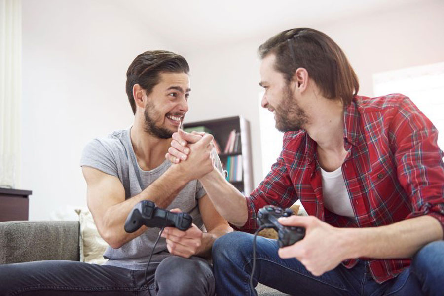 Two gamer friends holding each other’s hand while holding game controllers with their other hand.