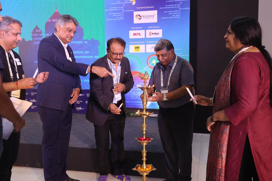 Five men wearing casual attire are standing together, likely at the IGDC Dev Day 2024 event. Some are wearing Karnavati University shirts and lanyards.